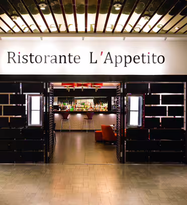 Entrance to Ristorante LAppetito with a modern design featuring black and white decor. Double doors open to reveal a stylish interior bar area with stools and warm lighting.